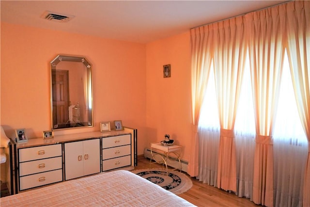 bedroom featuring light wood-type flooring, a baseboard radiator, and multiple windows