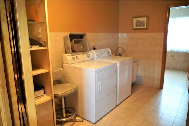 clothes washing area with washing machine and dryer, light tile patterned floors, and tile walls