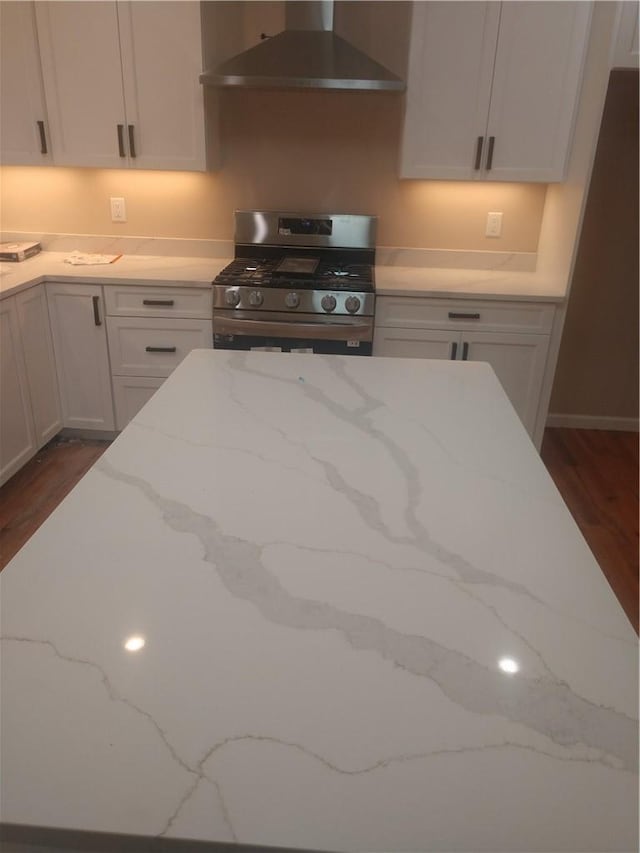 kitchen featuring stainless steel range with gas cooktop, wall chimney exhaust hood, light stone counters, and dark hardwood / wood-style floors