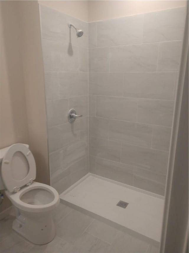 bathroom featuring tile patterned flooring, toilet, and tiled shower