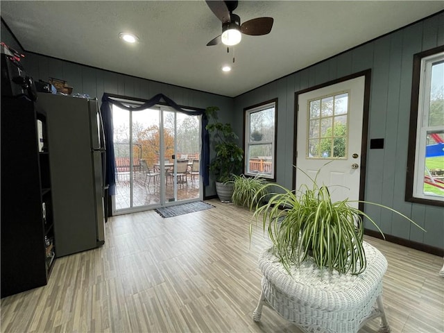 interior space with a textured ceiling, ceiling fan, light hardwood / wood-style flooring, and wood walls