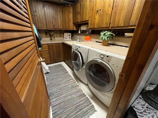 laundry area with washer and clothes dryer, cabinets, sink, wooden walls, and light tile patterned flooring