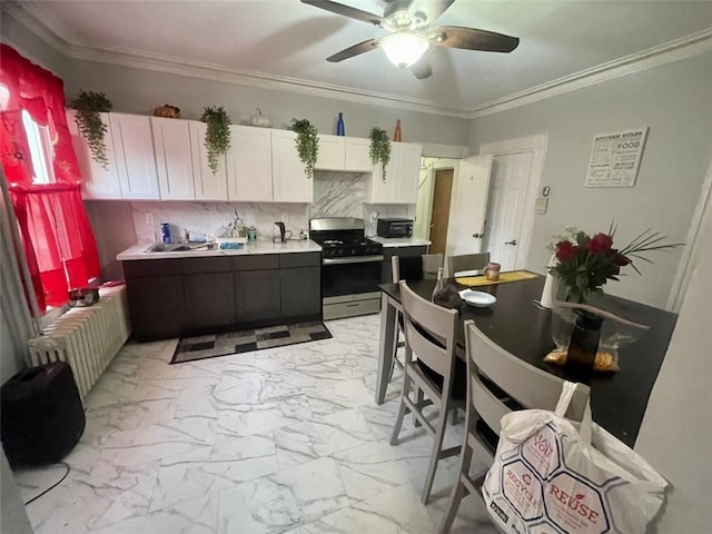 kitchen with stainless steel gas range oven, radiator, decorative backsplash, ornamental molding, and white cabinetry