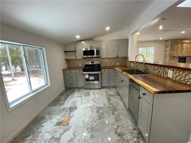 kitchen featuring sink, vaulted ceiling, gray cabinets, butcher block countertops, and stainless steel appliances