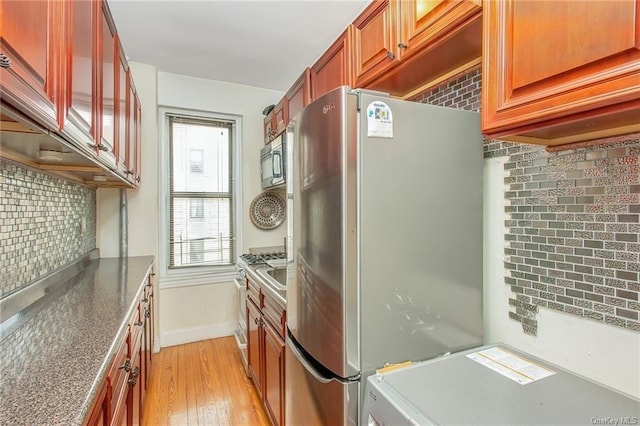 kitchen with light hardwood / wood-style flooring, dark stone countertops, backsplash, and stainless steel appliances