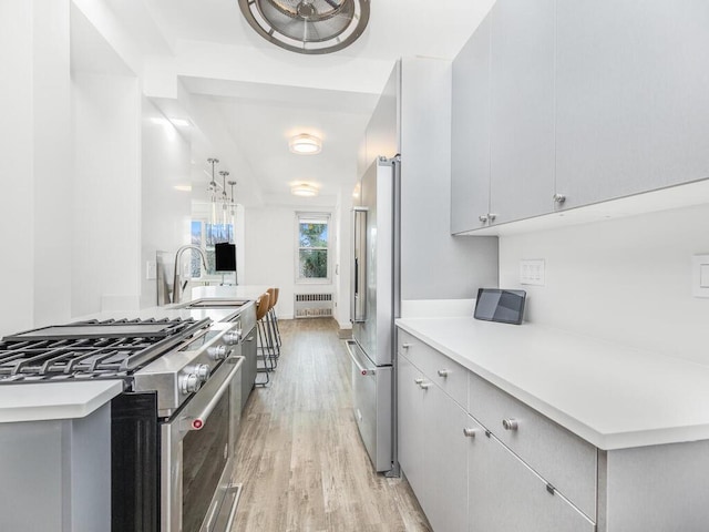 kitchen featuring high end appliances, sink, radiator heating unit, gray cabinets, and light wood-type flooring