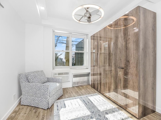 living area with light wood-type flooring, an AC wall unit, radiator, and ceiling fan