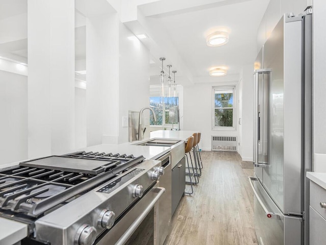 kitchen featuring a kitchen breakfast bar, radiator, high end appliances, light hardwood / wood-style flooring, and hanging light fixtures