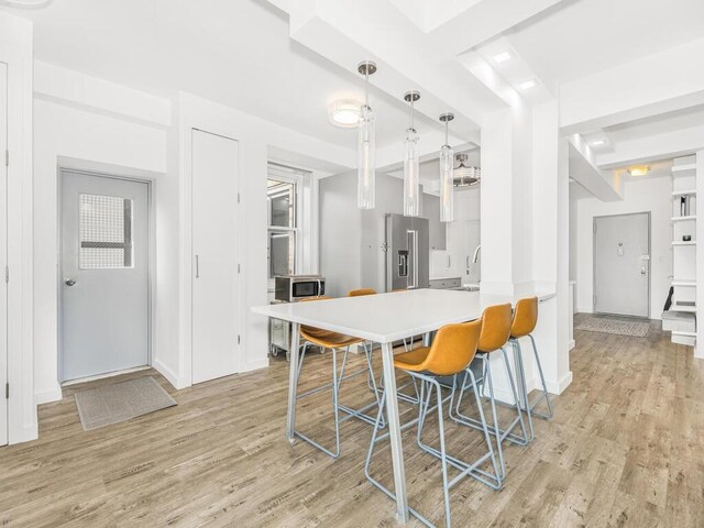 kitchen with a kitchen bar, stainless steel appliances, light hardwood / wood-style floors, white cabinetry, and hanging light fixtures