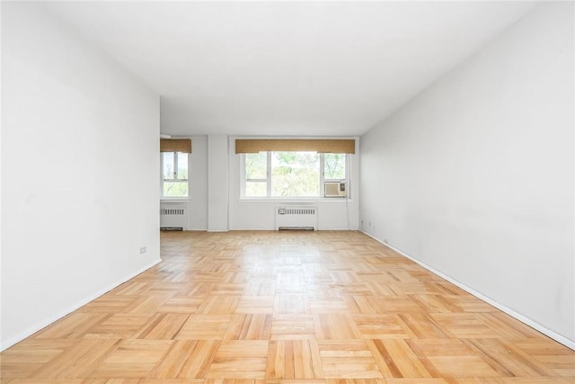 empty room with cooling unit, radiator heating unit, and light parquet flooring