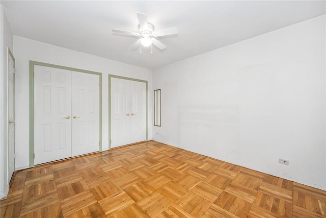 unfurnished bedroom featuring two closets, light parquet floors, and ceiling fan