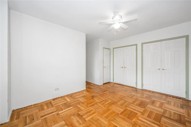 unfurnished bedroom with ceiling fan, two closets, and light parquet floors