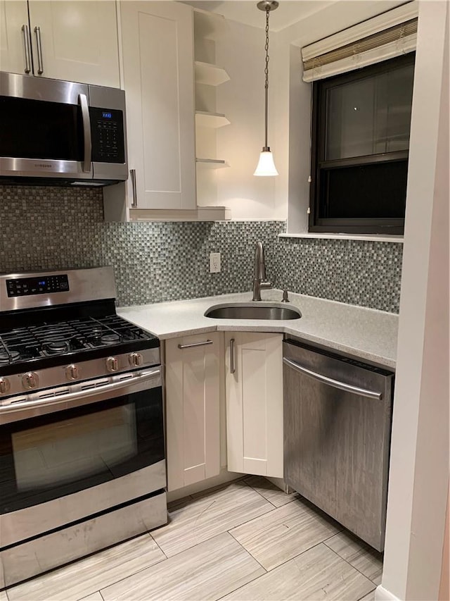 kitchen featuring sink, stainless steel appliances, pendant lighting, decorative backsplash, and light wood-type flooring