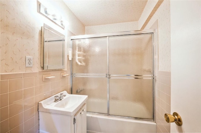 bathroom with a textured ceiling, vanity, tile walls, and enclosed tub / shower combo