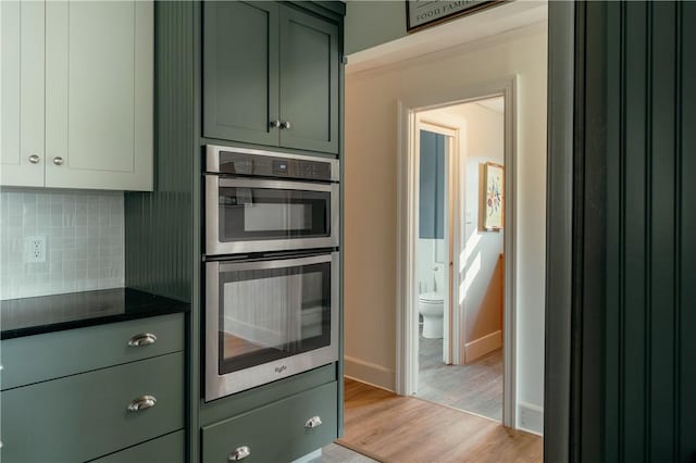 kitchen with backsplash, stainless steel double oven, light wood-type flooring, and green cabinetry