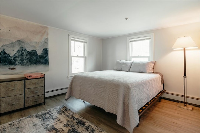 bedroom featuring wood-type flooring, multiple windows, and a baseboard heating unit