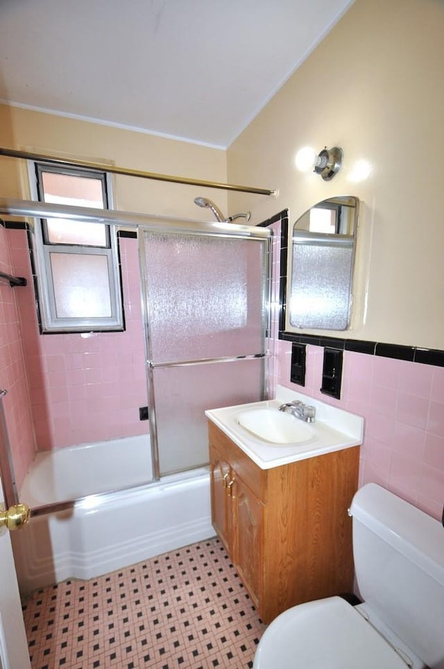 full bathroom featuring bath / shower combo with glass door, vaulted ceiling, toilet, vanity, and tile walls