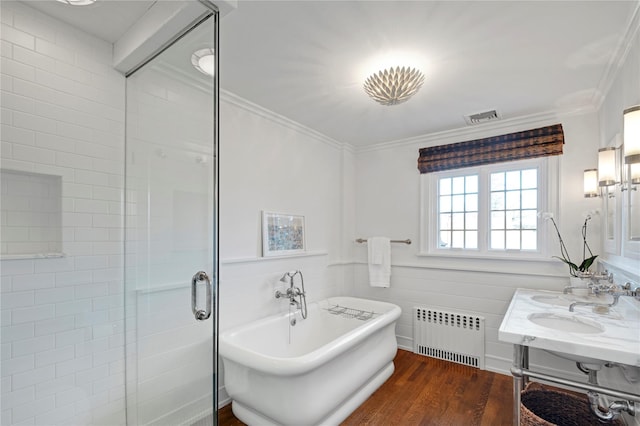 bathroom featuring dual sinks, radiator, crown molding, wood-type flooring, and separate shower and tub