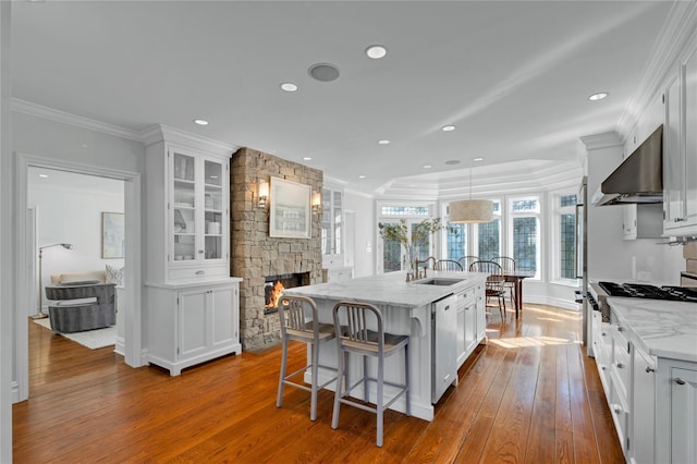 kitchen with wall chimney exhaust hood, a center island with sink, stainless steel dishwasher, pendant lighting, and white cabinets