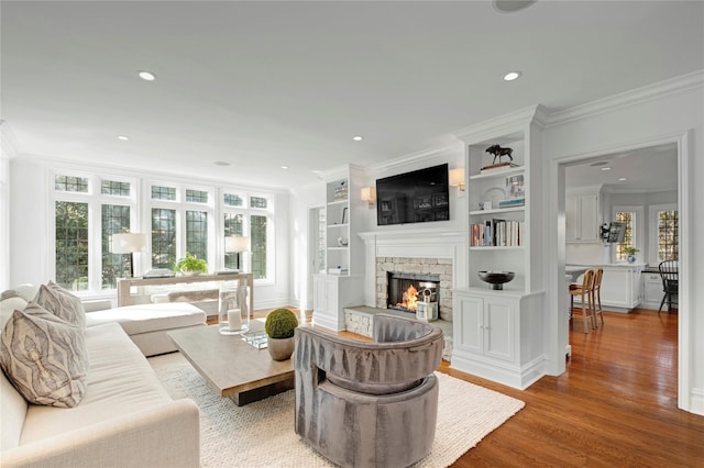 living room with wood-type flooring, a stone fireplace, and ornamental molding