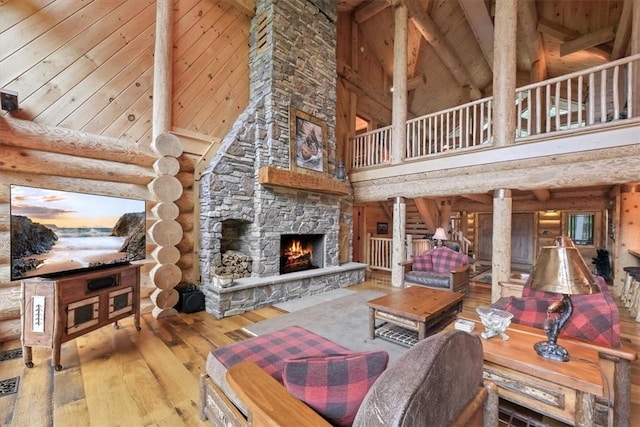 living room featuring a towering ceiling, ornate columns, log walls, wood-type flooring, and a stone fireplace