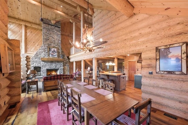 dining area with a fireplace, wood-type flooring, rustic walls, and beam ceiling