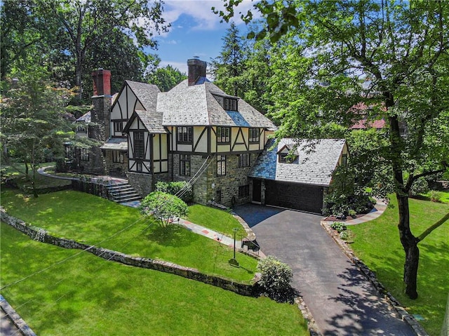 tudor house featuring aphalt driveway, a chimney, a front lawn, and stucco siding