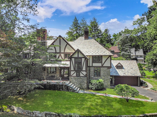 tudor home with driveway, stucco siding, a chimney, a front yard, and a high end roof