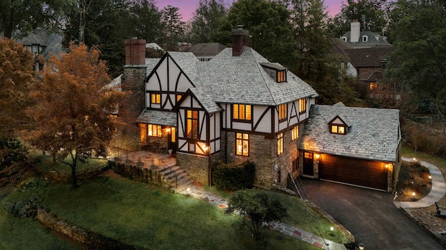 tudor house featuring driveway, stone siding, a lawn, stucco siding, and a chimney