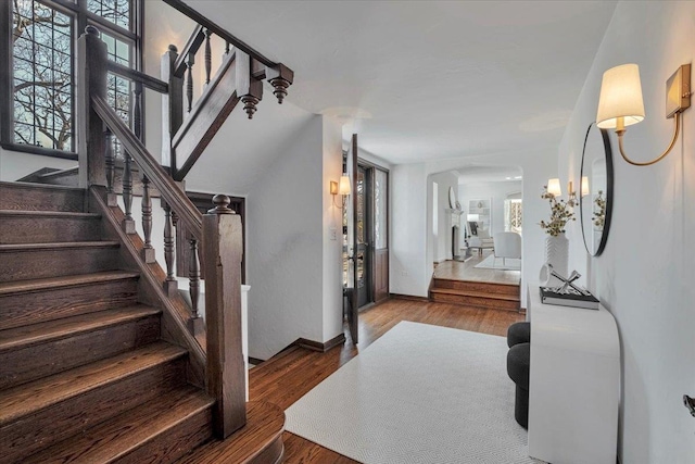 foyer entrance featuring stairs, arched walkways, wood finished floors, and a wealth of natural light