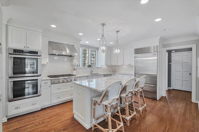 kitchen with appliances with stainless steel finishes, white cabinetry, a sink, and wall chimney range hood