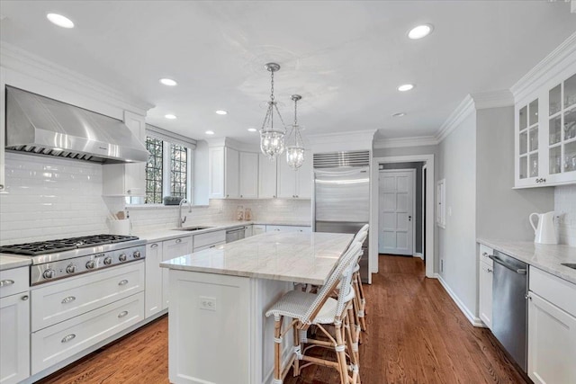 kitchen with wall chimney exhaust hood, appliances with stainless steel finishes, crown molding, white cabinetry, and a sink