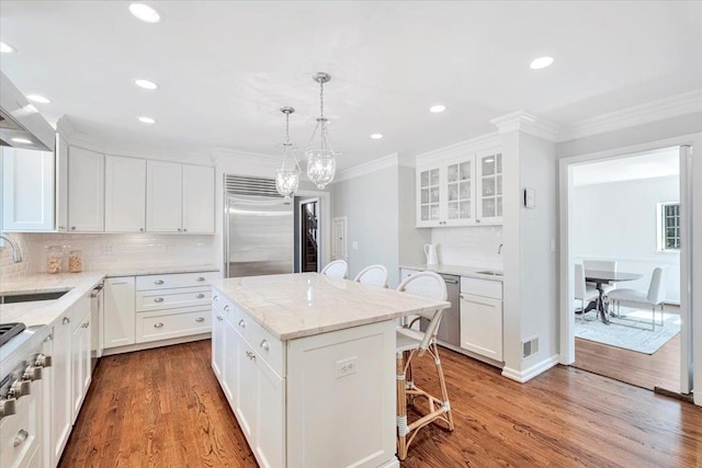 kitchen featuring a kitchen island, stainless steel appliances, crown molding, white cabinetry, and a sink