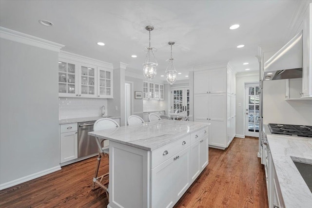 kitchen with stainless steel dishwasher, glass insert cabinets, white cabinets, under cabinet range hood, and a kitchen breakfast bar