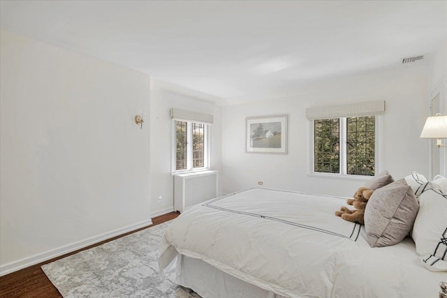 bedroom featuring radiator heating unit, wood finished floors, visible vents, and baseboards