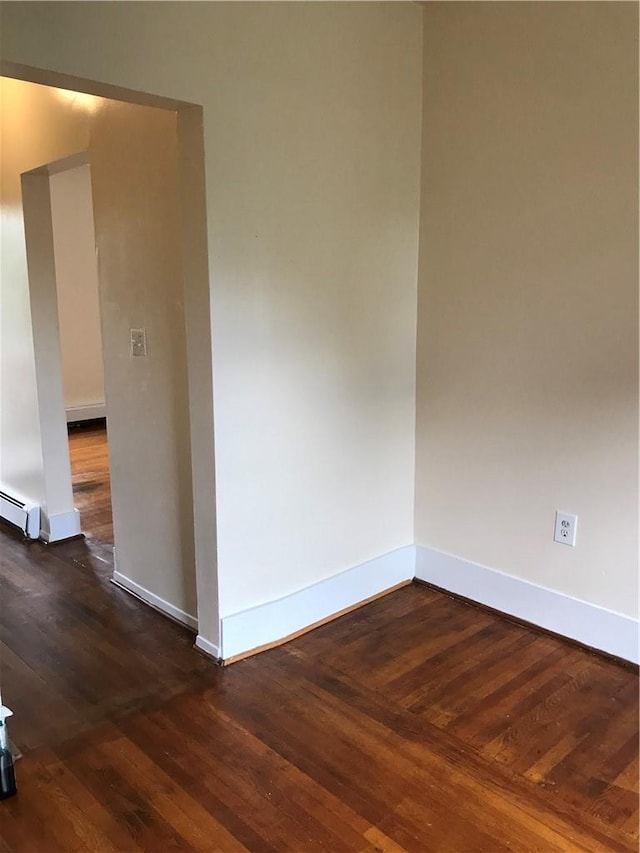 empty room with dark wood-type flooring and a baseboard heating unit