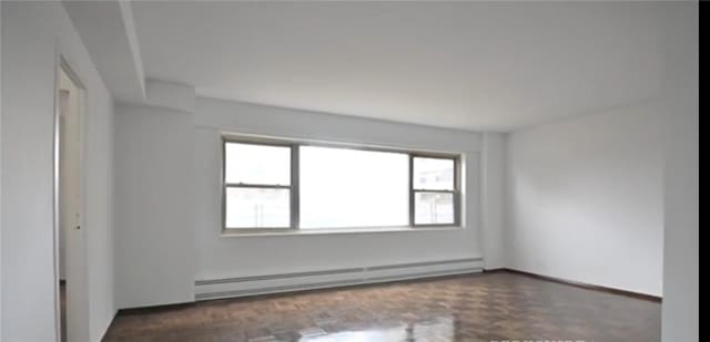 spare room featuring baseboard heating and dark parquet floors