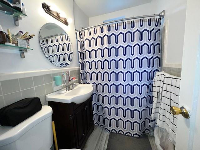 bathroom with a shower with curtain, vanity, toilet, and tile walls