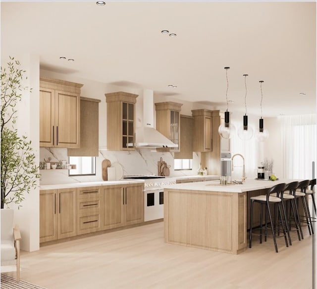 kitchen with sink, wall chimney range hood, light hardwood / wood-style flooring, an island with sink, and light brown cabinetry