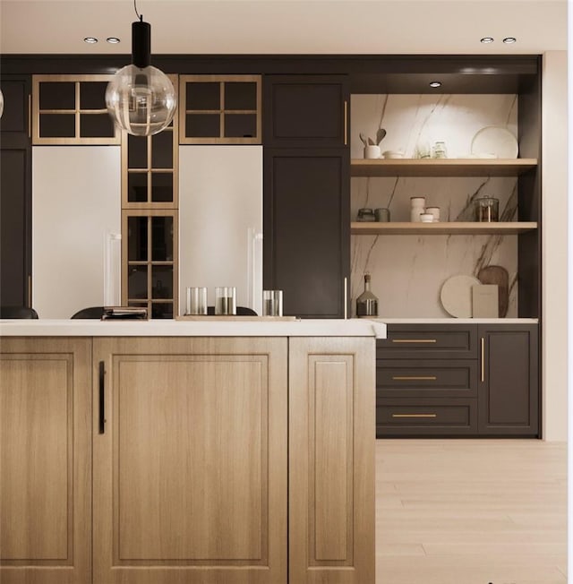 bar with light brown cabinets, hanging light fixtures, and light hardwood / wood-style flooring