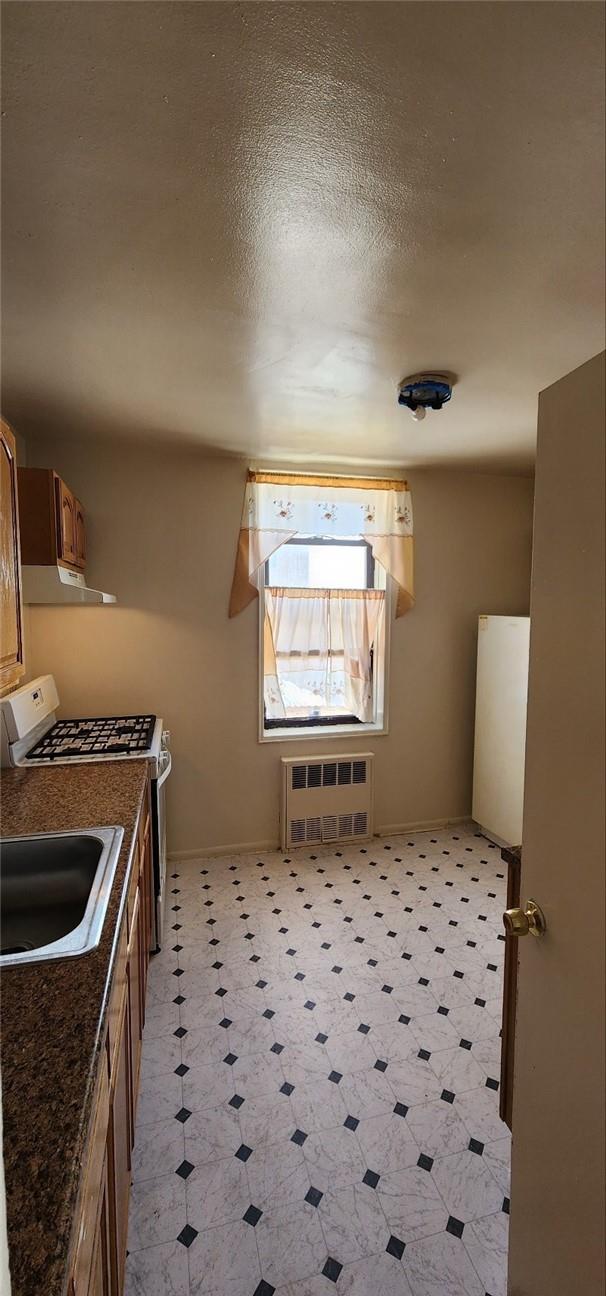 kitchen with a textured ceiling, heating unit, white range with electric cooktop, and sink