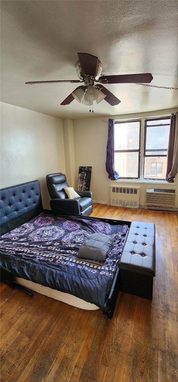 interior space with an AC wall unit, hardwood / wood-style flooring, ceiling fan, a textured ceiling, and radiator heating unit