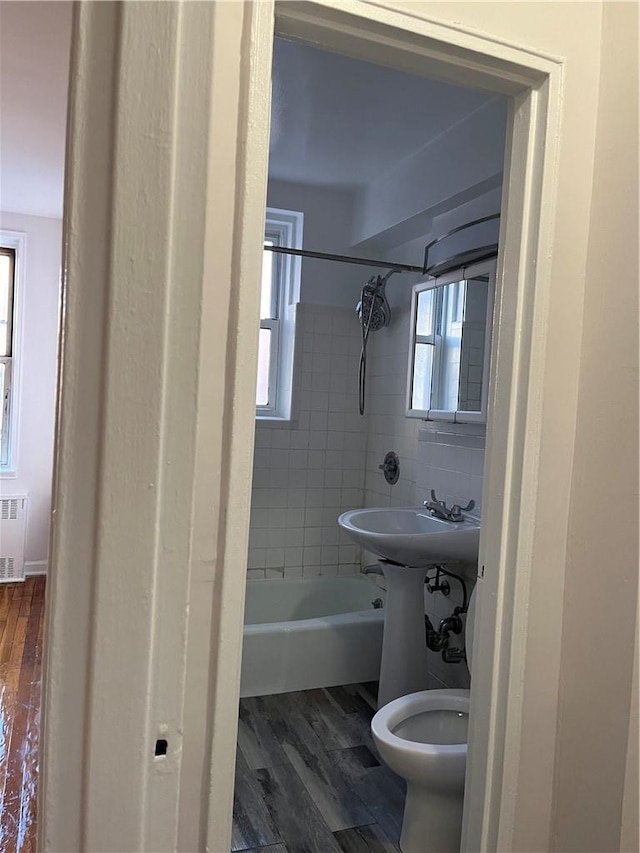 full bathroom featuring hardwood / wood-style floors, sink, tiled shower / bath combo, toilet, and radiator heating unit