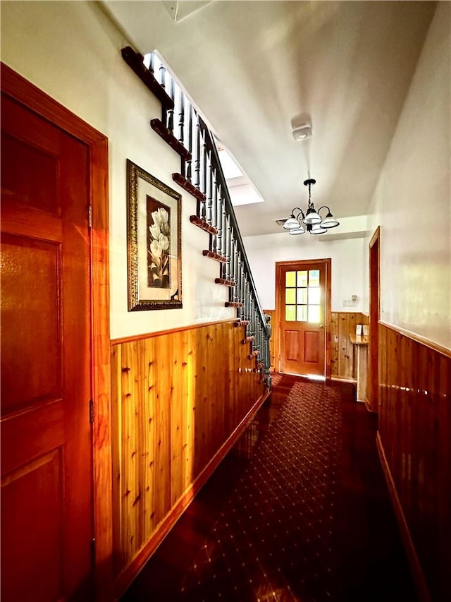 hall featuring wood walls and a chandelier