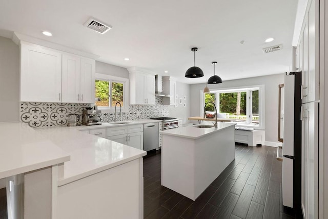 kitchen with pendant lighting, sink, wall chimney exhaust hood, white cabinetry, and stainless steel appliances