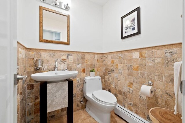 bathroom featuring sink, toilet, baseboard heating, and tile walls