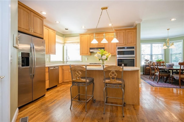 kitchen featuring decorative light fixtures, a center island, stainless steel appliances, and plenty of natural light