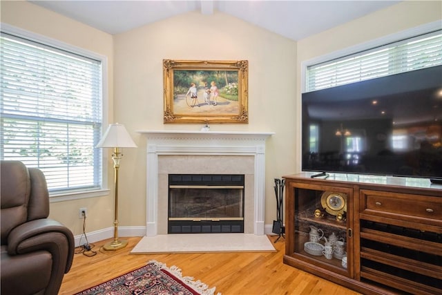 living area featuring hardwood / wood-style flooring, lofted ceiling with beams, a healthy amount of sunlight, and a high end fireplace