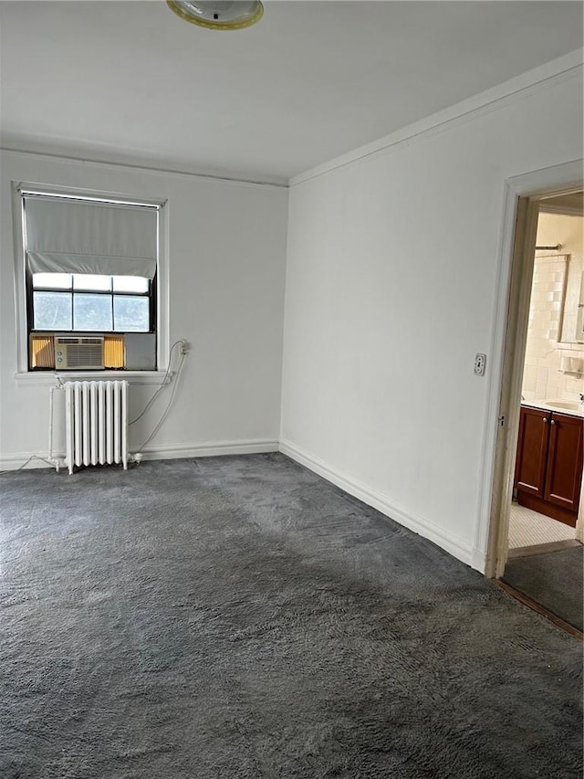 empty room with cooling unit, crown molding, sink, dark colored carpet, and radiator heating unit