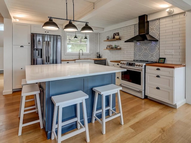 kitchen featuring pendant lighting, white cabinets, wall chimney range hood, range with electric cooktop, and stainless steel fridge with ice dispenser